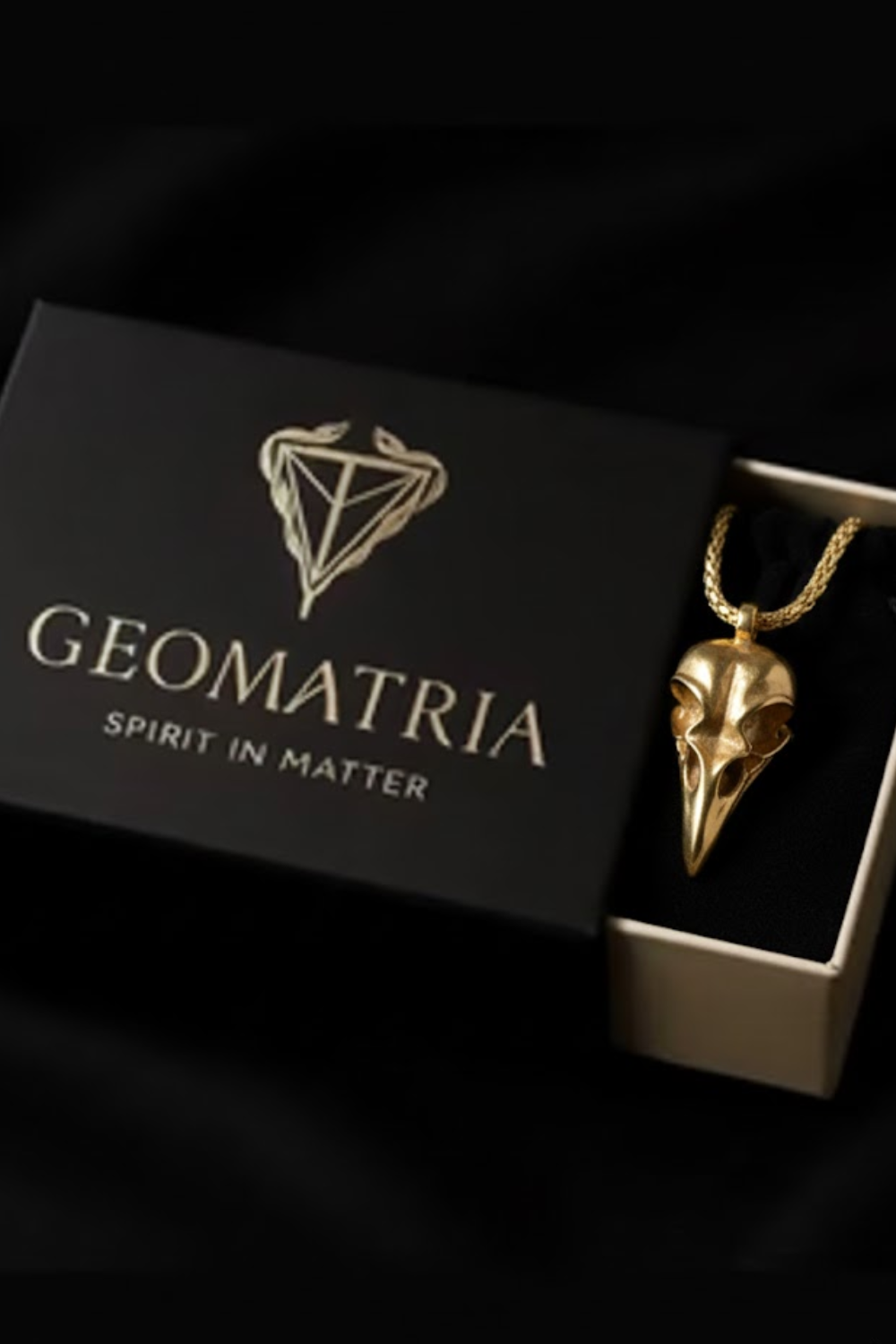 A gold bird pendant is displayed in a black box with the text "Geomatria" and "SPIRIT IN MATTERS" printed on it.
