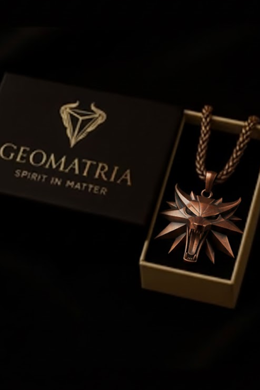 A pendant necklace with a metallic wolf head pendant is displayed in a box with the Geomatria logo, and the box is placed on a black background.
