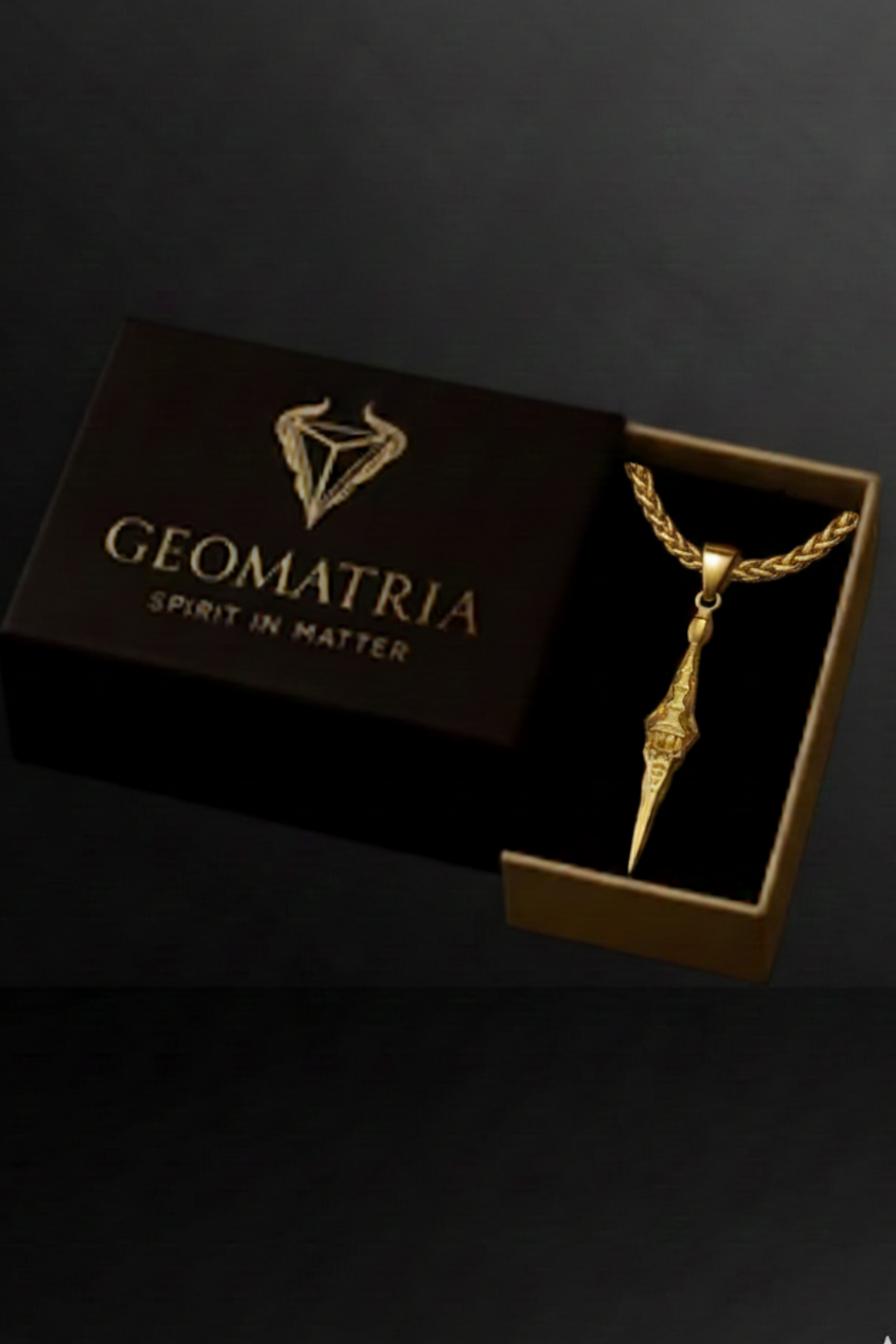 A gold necklace with a pendant is displayed in an open gold box with the text "Geomatria" printed on it.