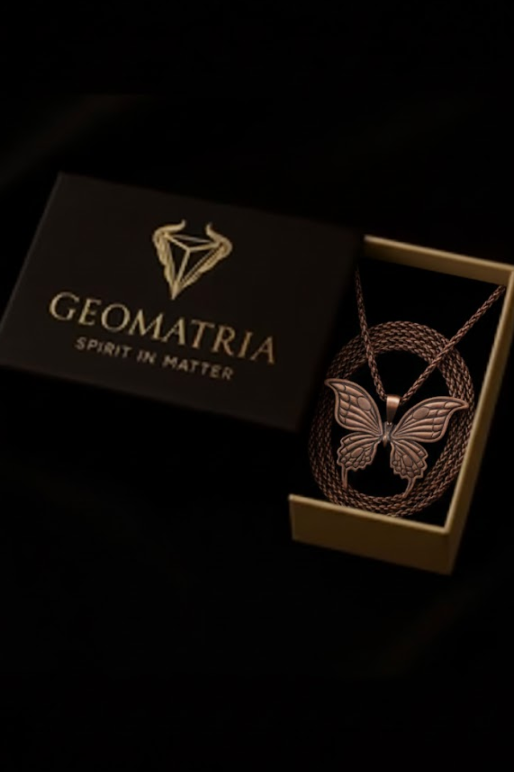 A necklace with a butterfly pendant is displayed in a black box with the text "Geomatria" and "Spirit in Matter" printed on it.