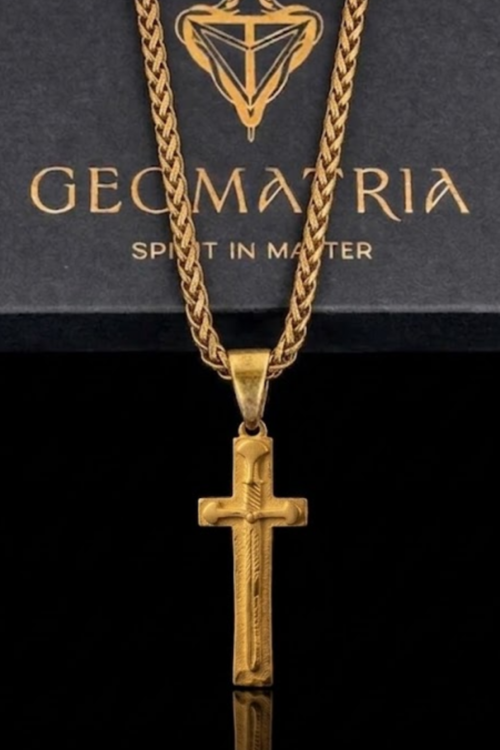 A gold-colored cross pendant with a braided chain is displayed against a black background.