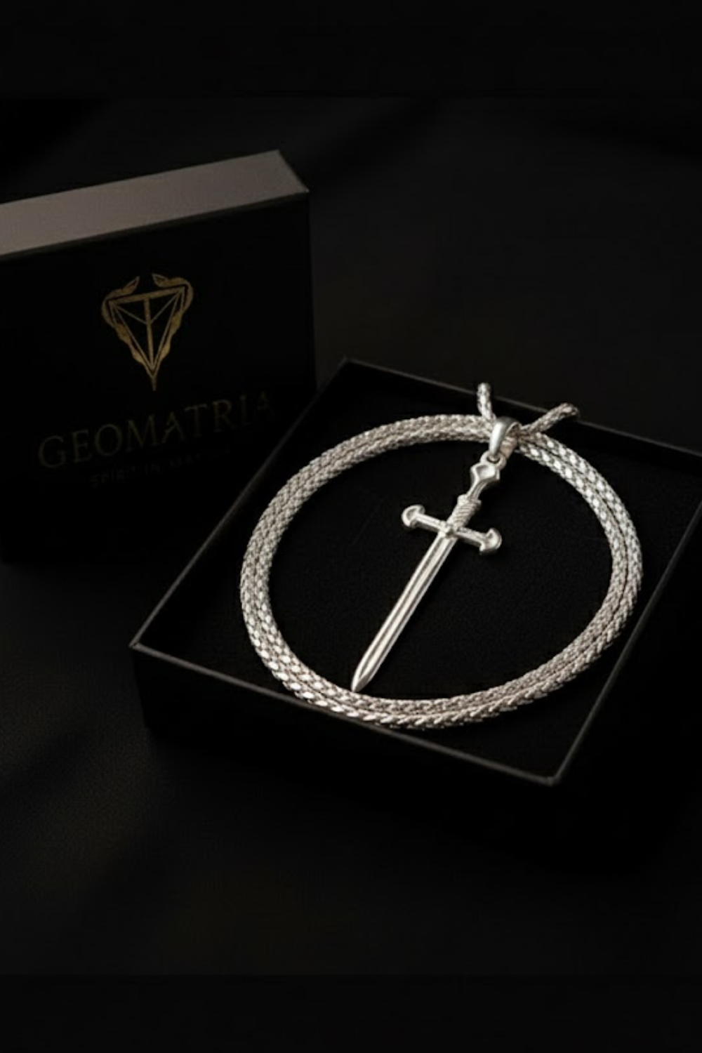 A silver sword pendant is displayed in a black jewelry box, with a silver chain around it.