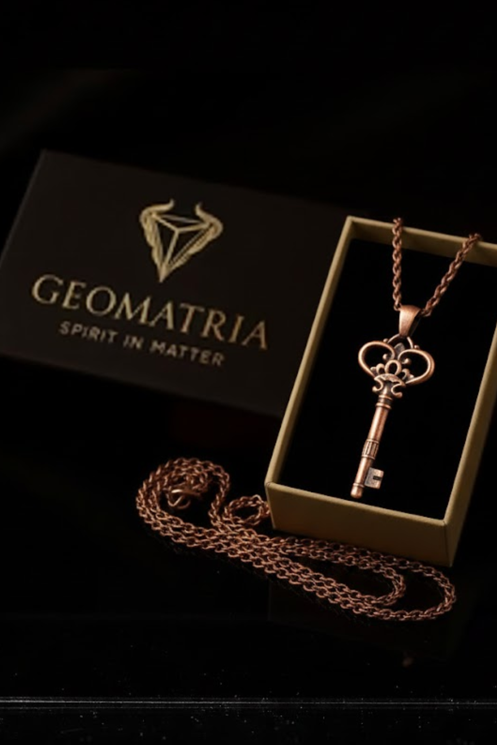 a necklace with a key pendant, placed inside a box with a key design, and a chain is visible on the table.