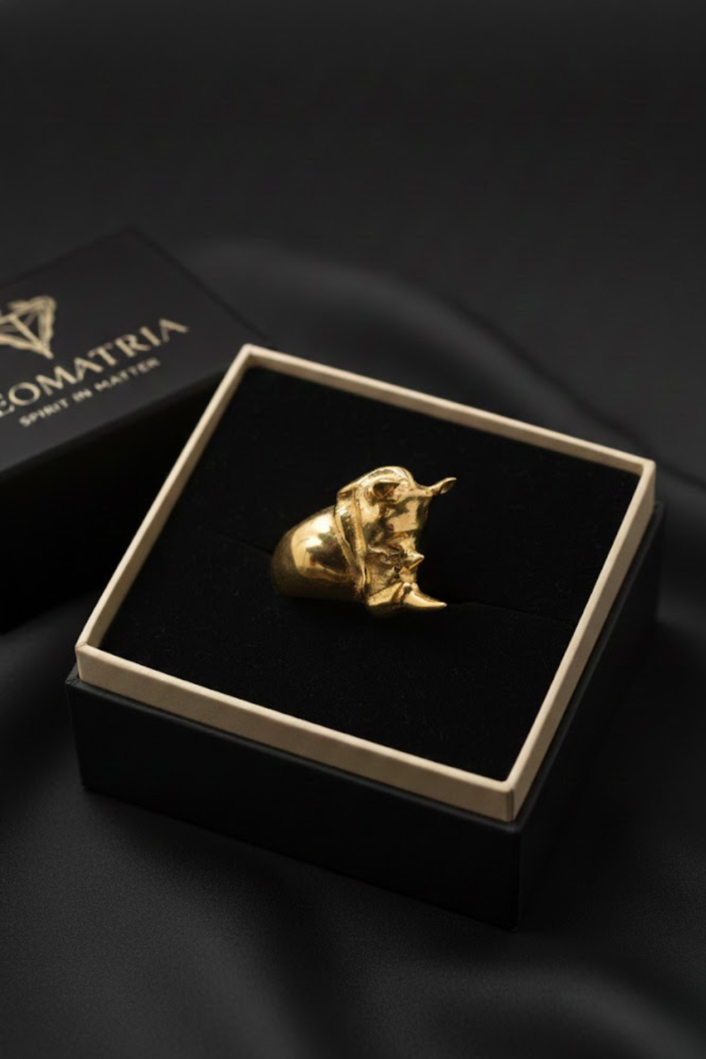A gold ring is displayed in a black box with a gold border, placed on a black surface.