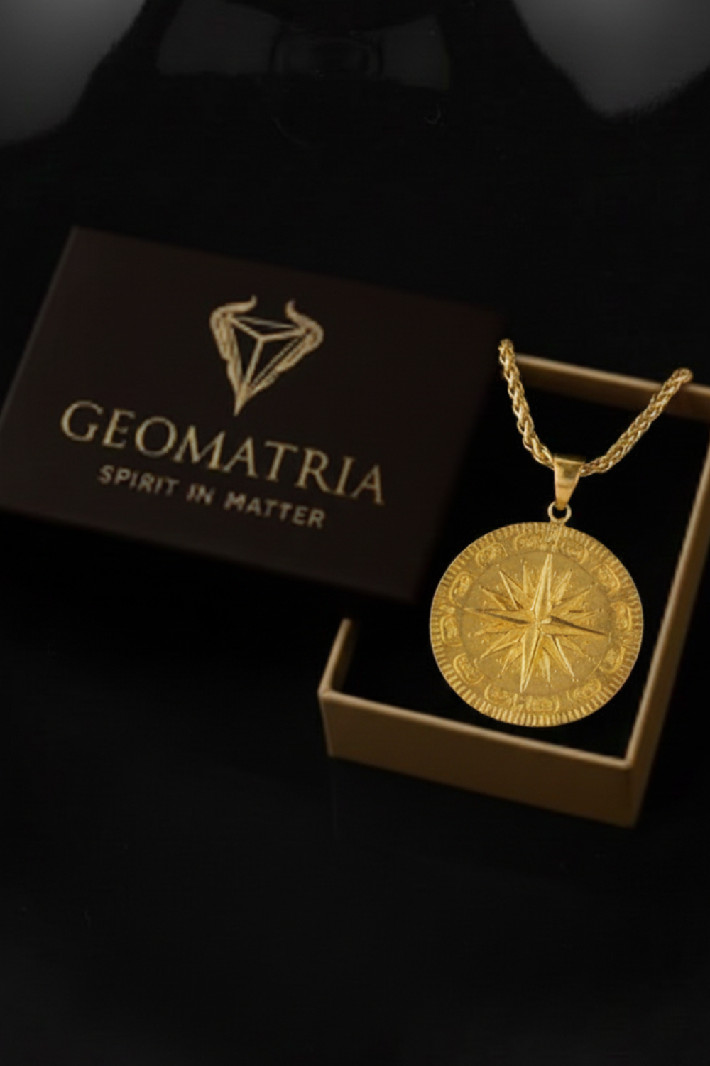 A gold compass pendant is displayed in a gold box with the text "Geomatria" and "SPIRIT IN MATTERS" printed on it.