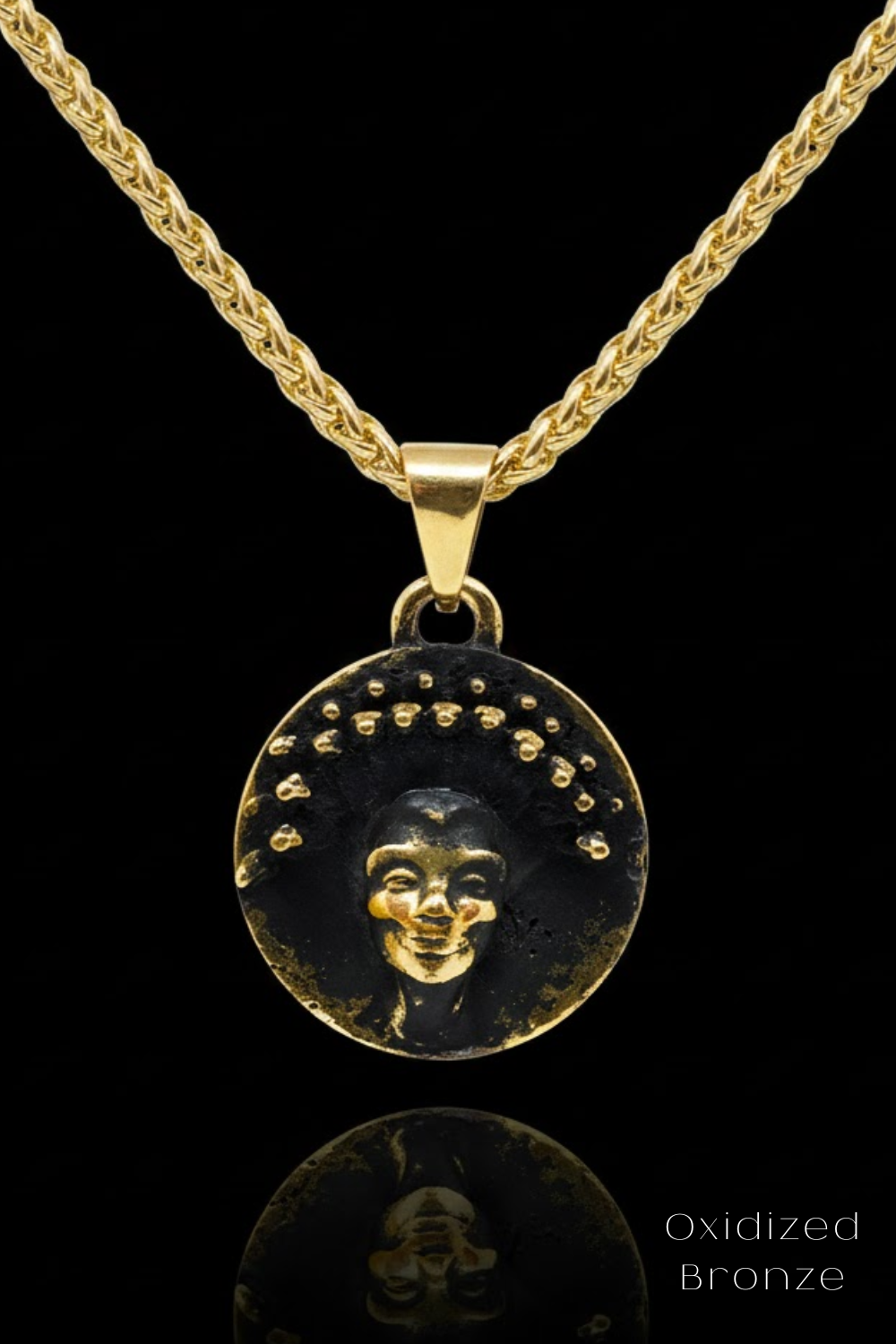 A gold-colored pendant necklace with a circular medallion featuring a face design.