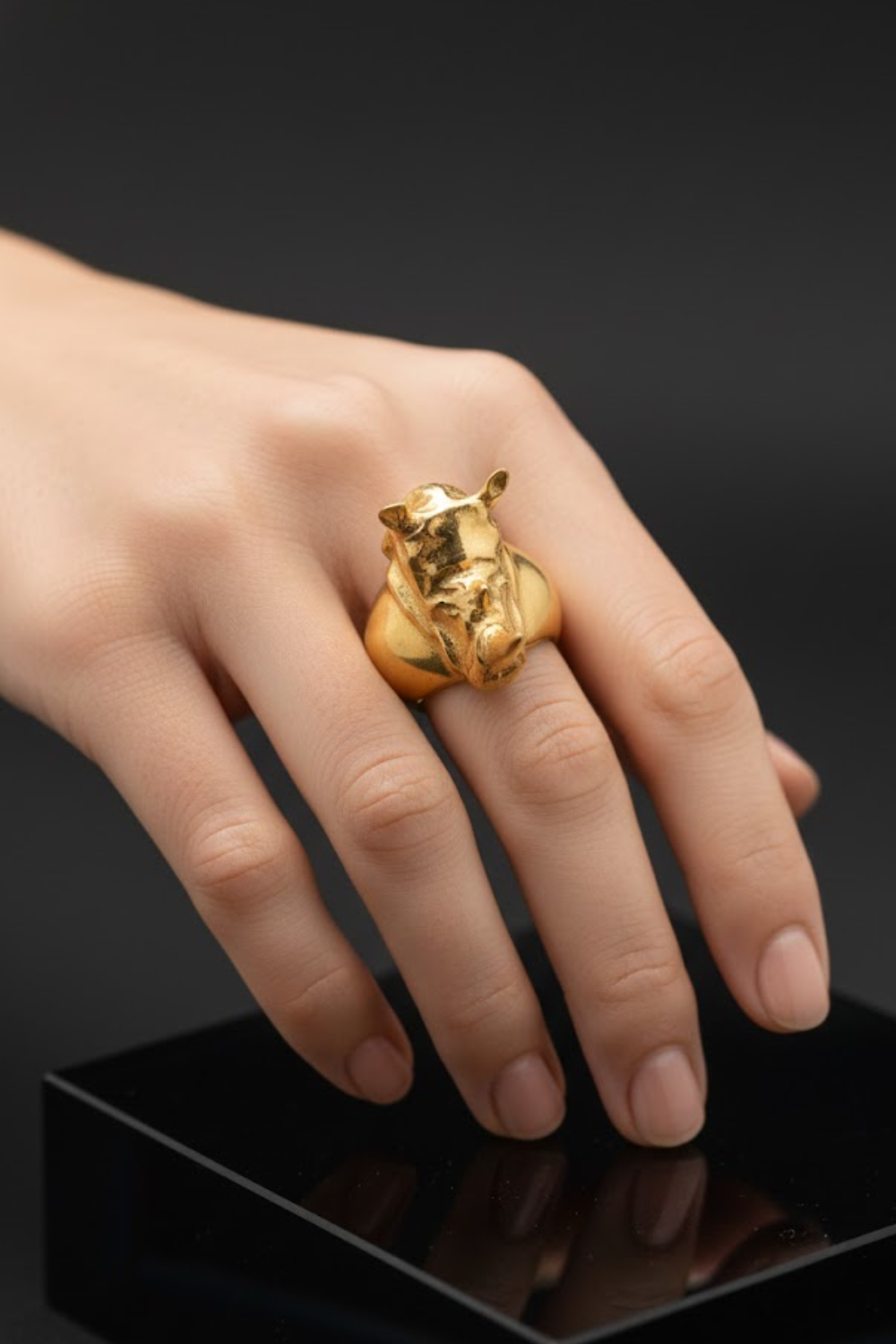 A close-up image of a person's hand wearing a gold ring with a pig head design.