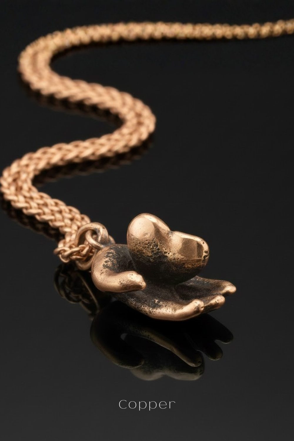 A close-up image of a gold-colored pendant with a heart-shaped design, hanging from a chain against a dark background.