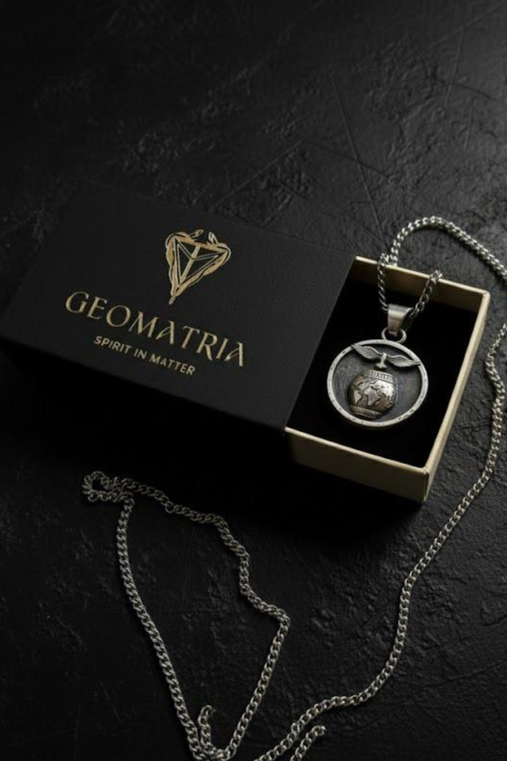 A pendant necklace with a pendant displayed in a black box with the text "Geomatria" and "Spirit in Matter" written on it.