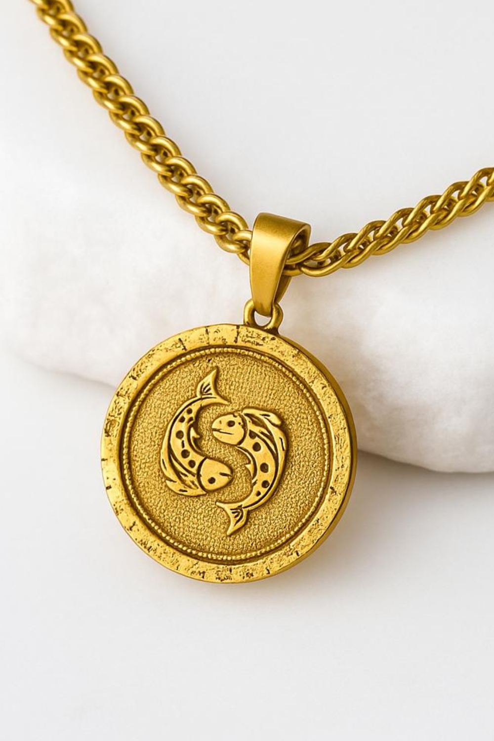 A gold-colored pendant with a circular design featuring two fish facing each other.
