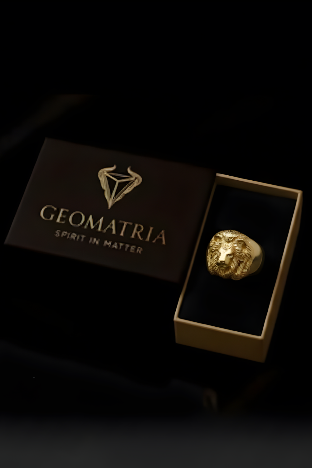 A gold ring is displayed in a gold box with the text "Geomatria" and "SPIRIT IN MATTER" printed on it.