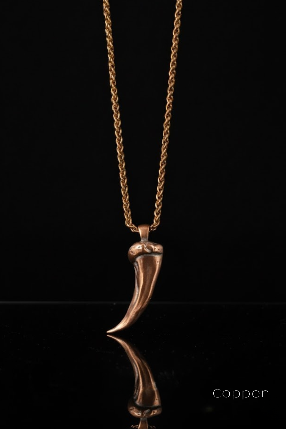 A copper-colored pendant necklace with a chain is displayed against a black background.