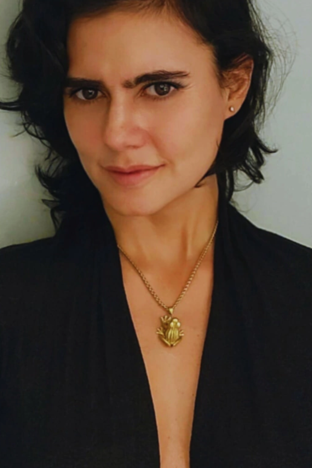 A woman with dark hair wearing a black top and a gold necklace with a pendant.