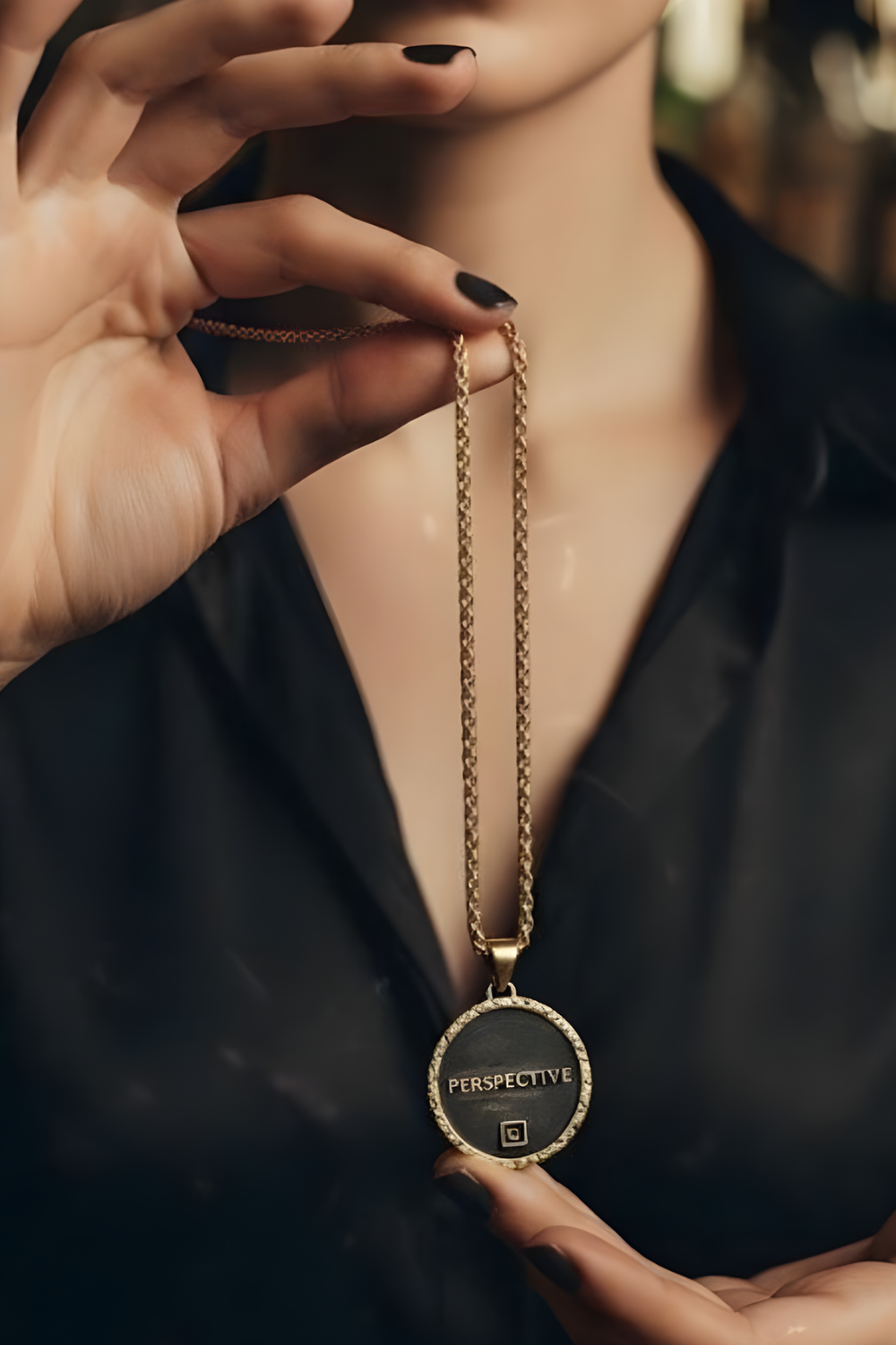 A close-up of a person's hand holding a gold chain necklace with a circular pendant that says "PERSPECTIVE".