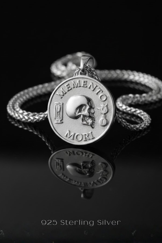 A silver medallion pendant with the Latin motto "Memento mori" engraved on it, hanging from a chain against a black background.