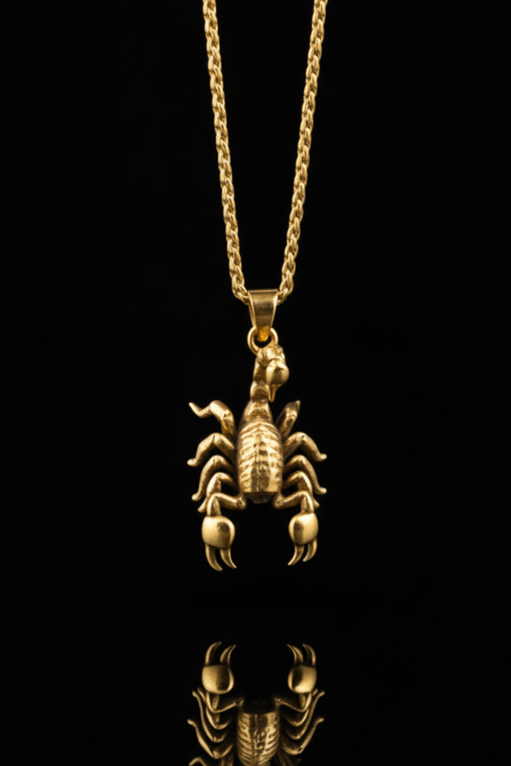 A gold-colored pendant in the shape of a scorpion is displayed against a black background, with its reflection visible below it.