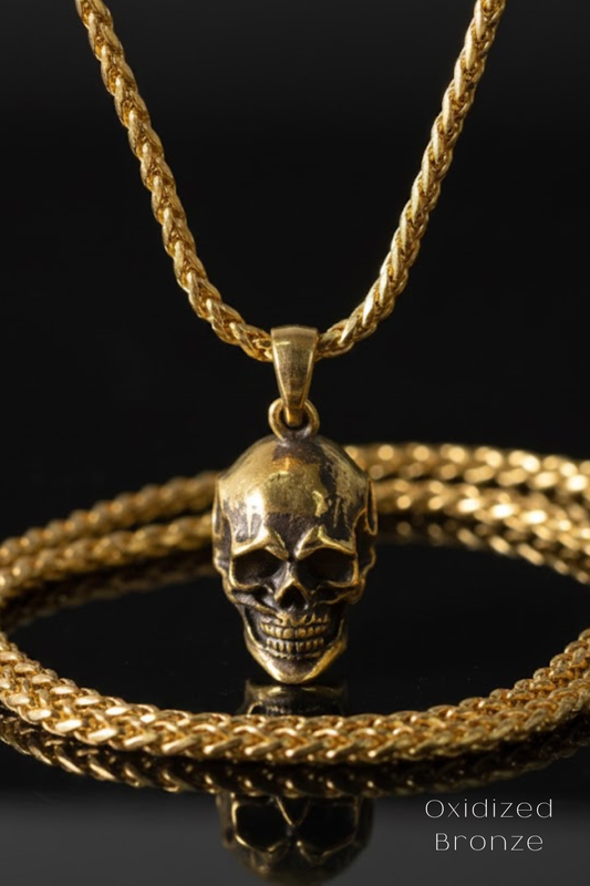 A gold-colored necklace with a pendant featuring a skull design, displayed against a black background.