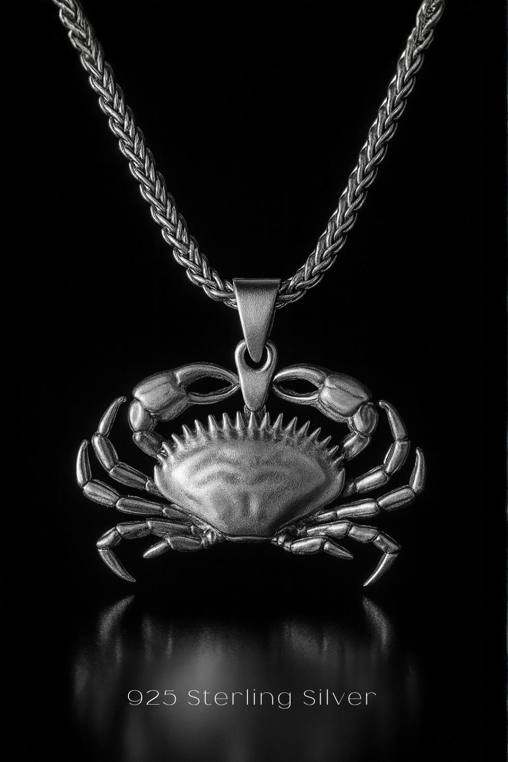 A silver-toned pendant featuring a detailed crab design, suspended from a chain against a black background.