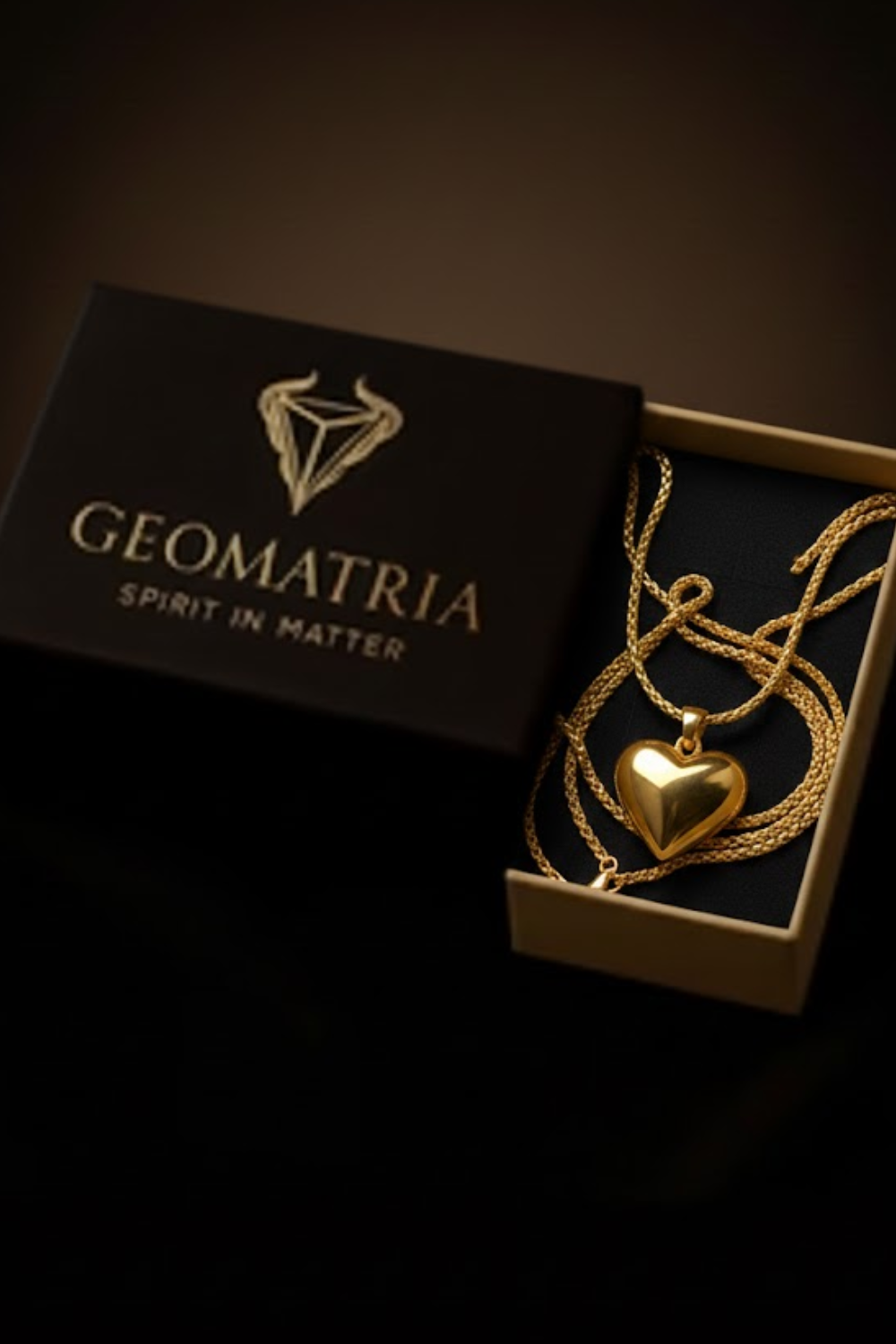 A gold heart-shaped pendant necklace is displayed in an open box with the brand name "Geomatria" printed on it.