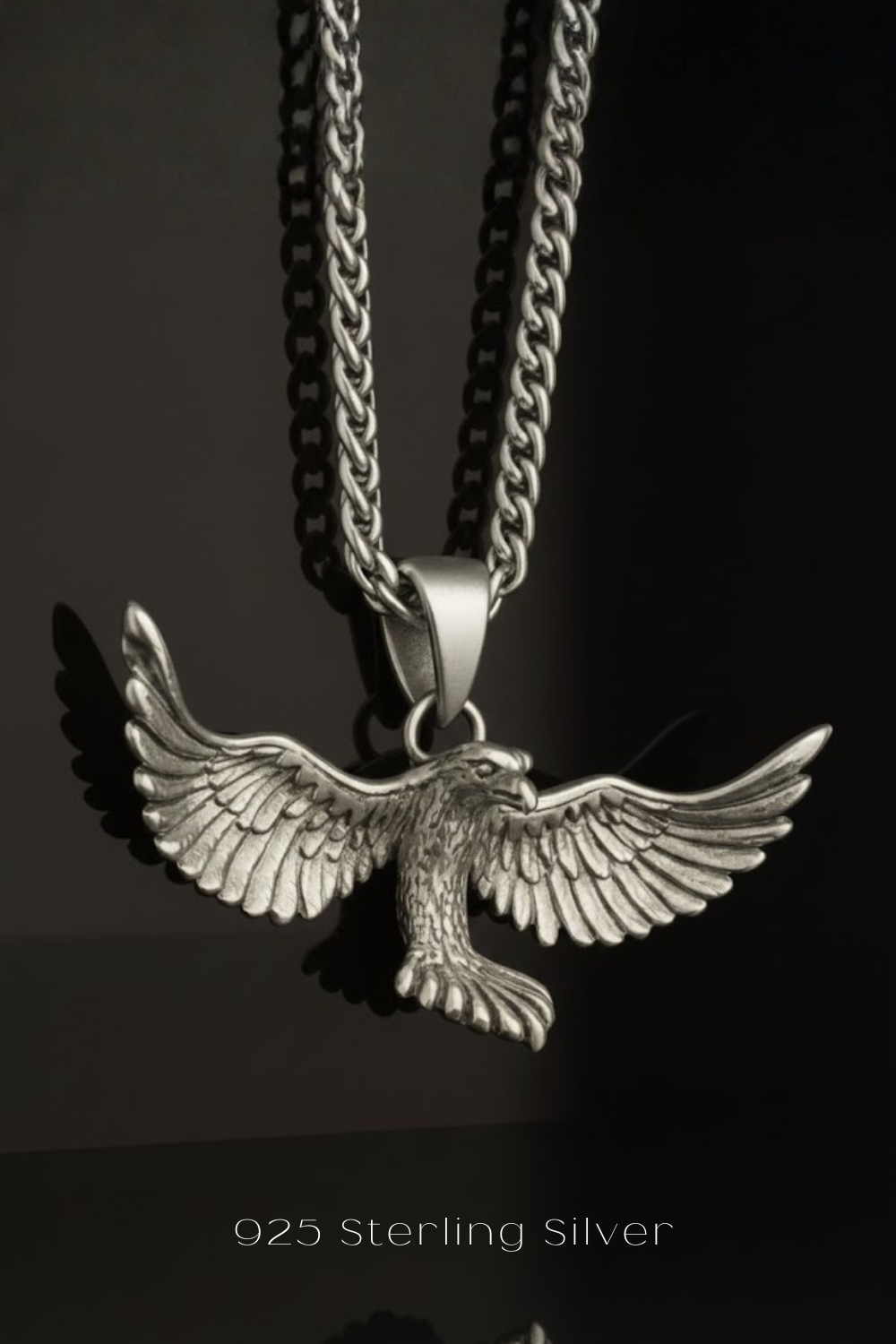 A silver-toned pendant necklace with a detailed eagle design, suspended against a dark background.