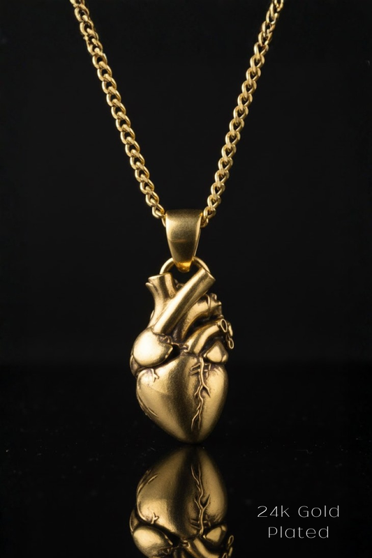 A 24K gold-plated pendant in the shape of a heart is displayed against a black background, with its reflection visible below it.