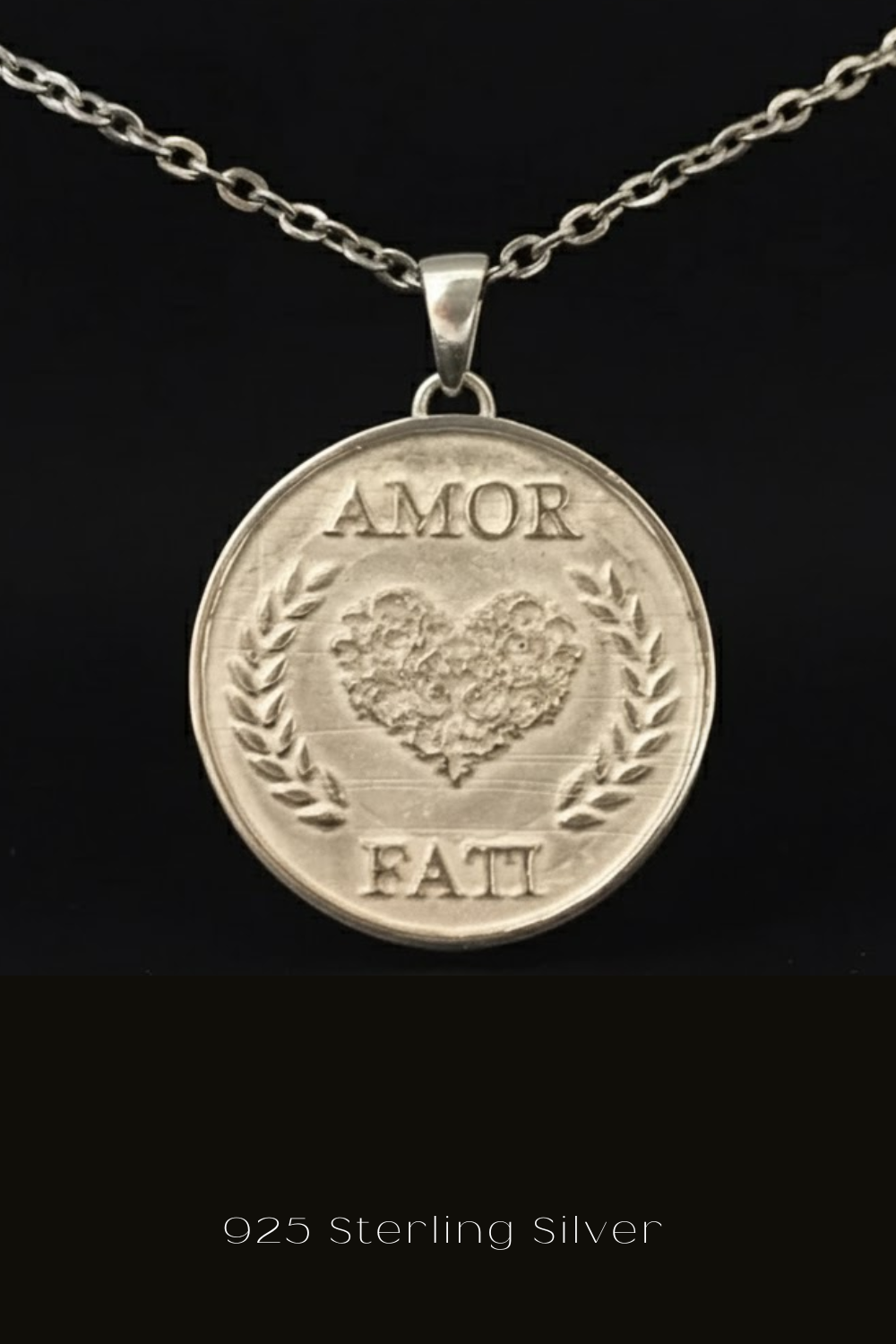 A silver pendant necklace with a round medallion-shaped pendant featuring the words "Amor Fati" and a heart design.