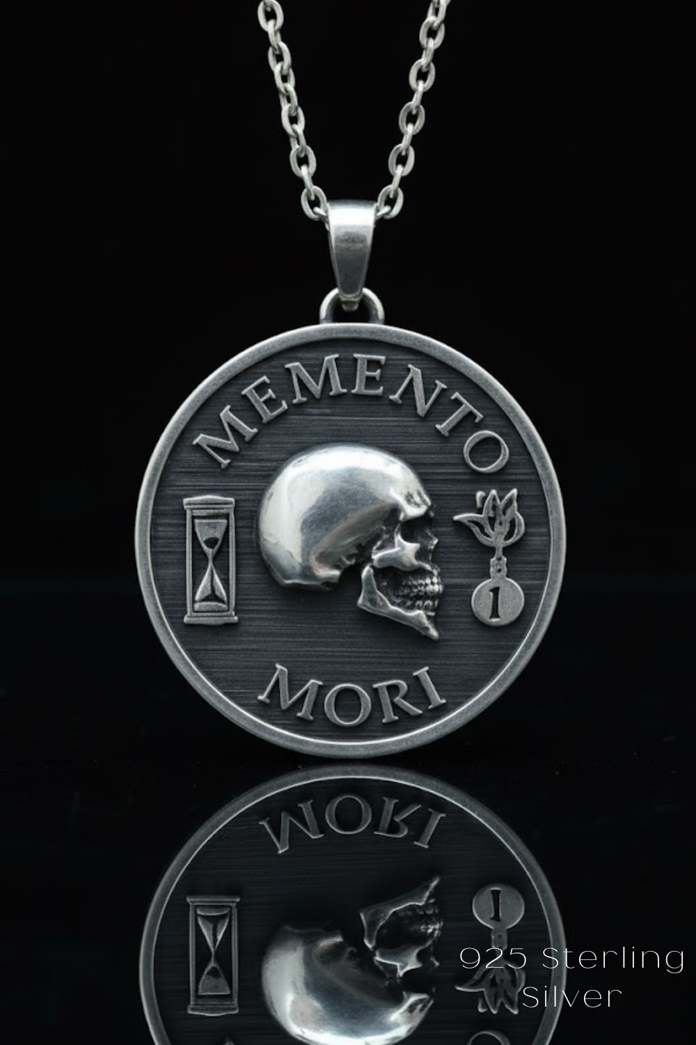 A silver pendant necklace with a circular medallion featuring a skull and the Latin phrase "Memento mori" (meaning remembrance of death ').