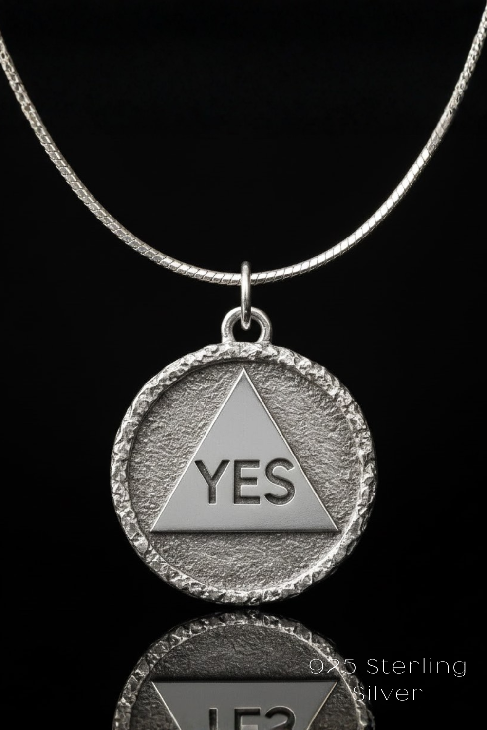 A silver-colored pendant necklace with a circular pendant featuring a triangle and the word "YES" engraved on it.