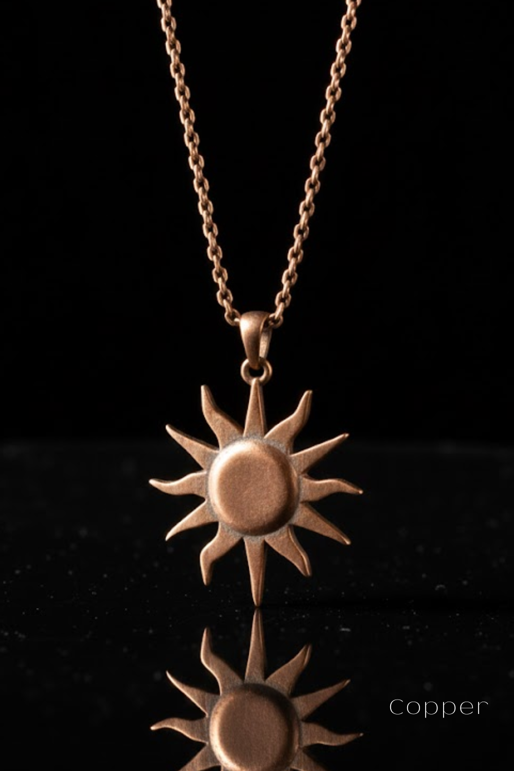 A copper-colored pendant necklace with a sun-shaped design is displayed against a black background.