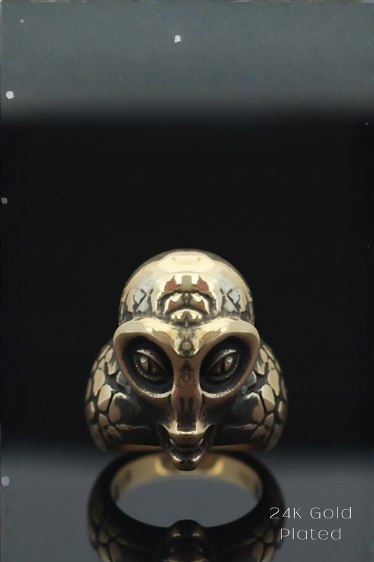 A gold ring with an intricate, alien-like design on the front, set against a black background.