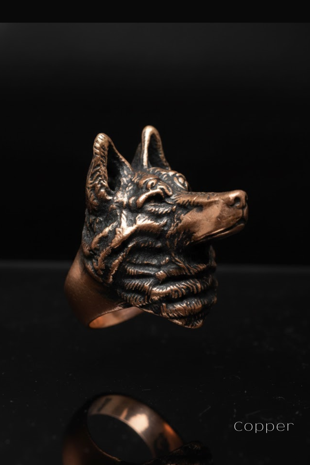 A close-up image of a copper-colored metal ring in the shape of a dog's head, with its eyes and ears visible.