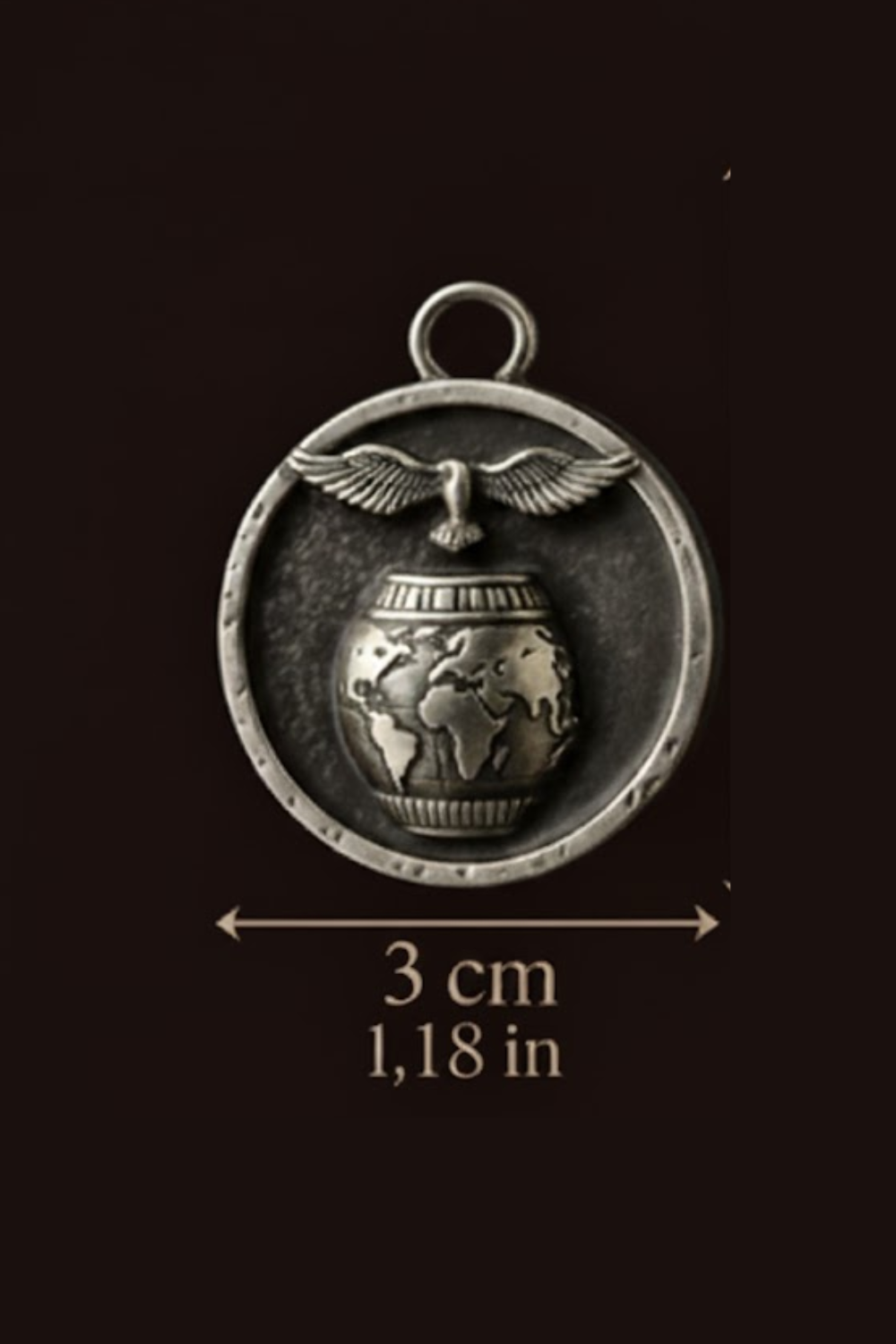 A silver-colored pendant with a world map design and a bird in flight, with the dimensions provided as 3 cm 1,18 in.
