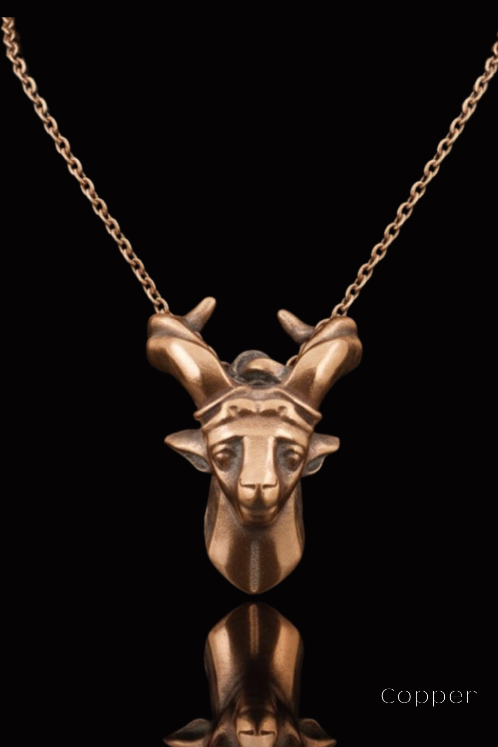 A copper-colored pendant in the shape of a deer head with antlers, suspended from a chain against a black background.