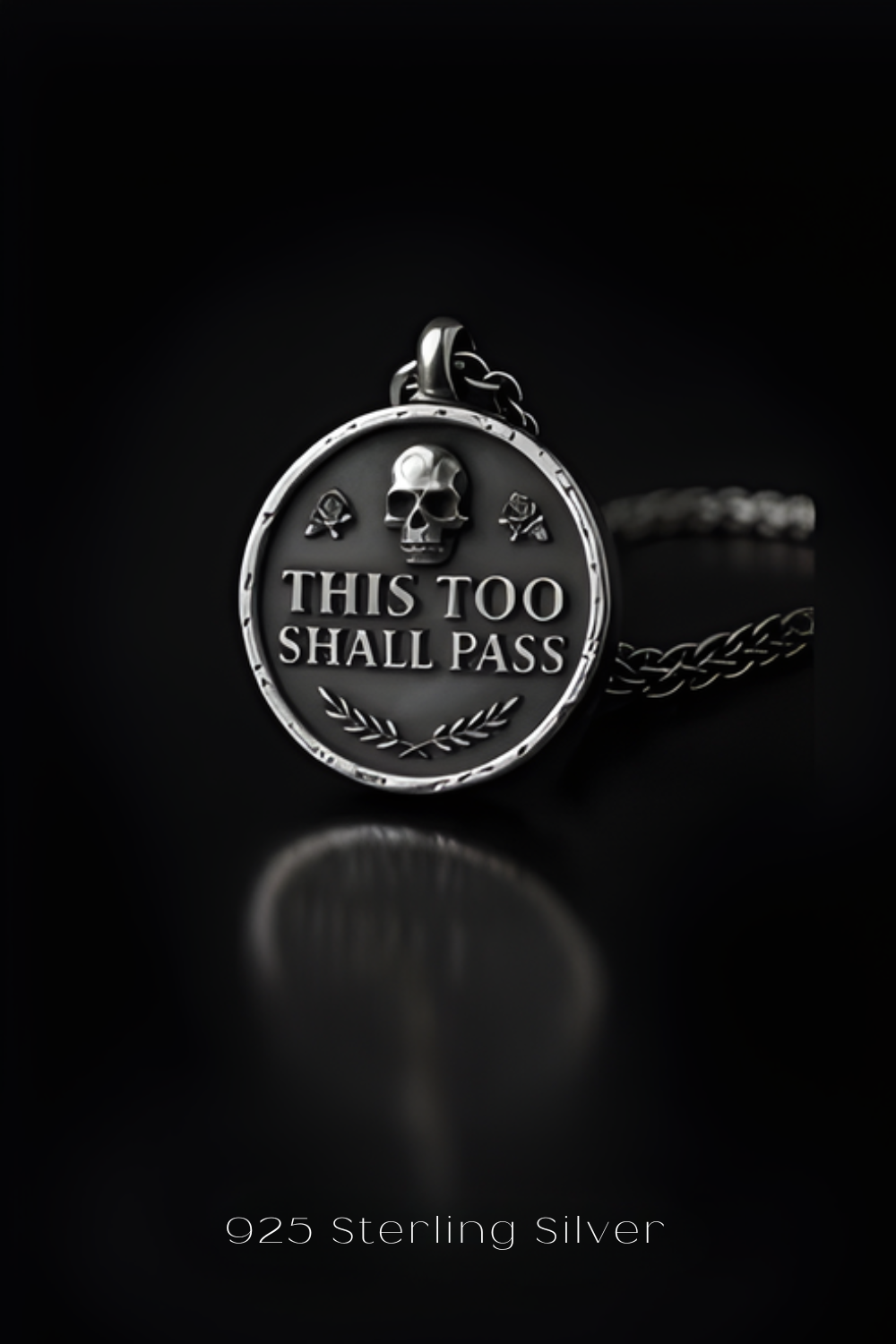 A silver pendant with the text "THIS TOO SHALL PASS" engraved on it, surrounded by a skull and rose design.