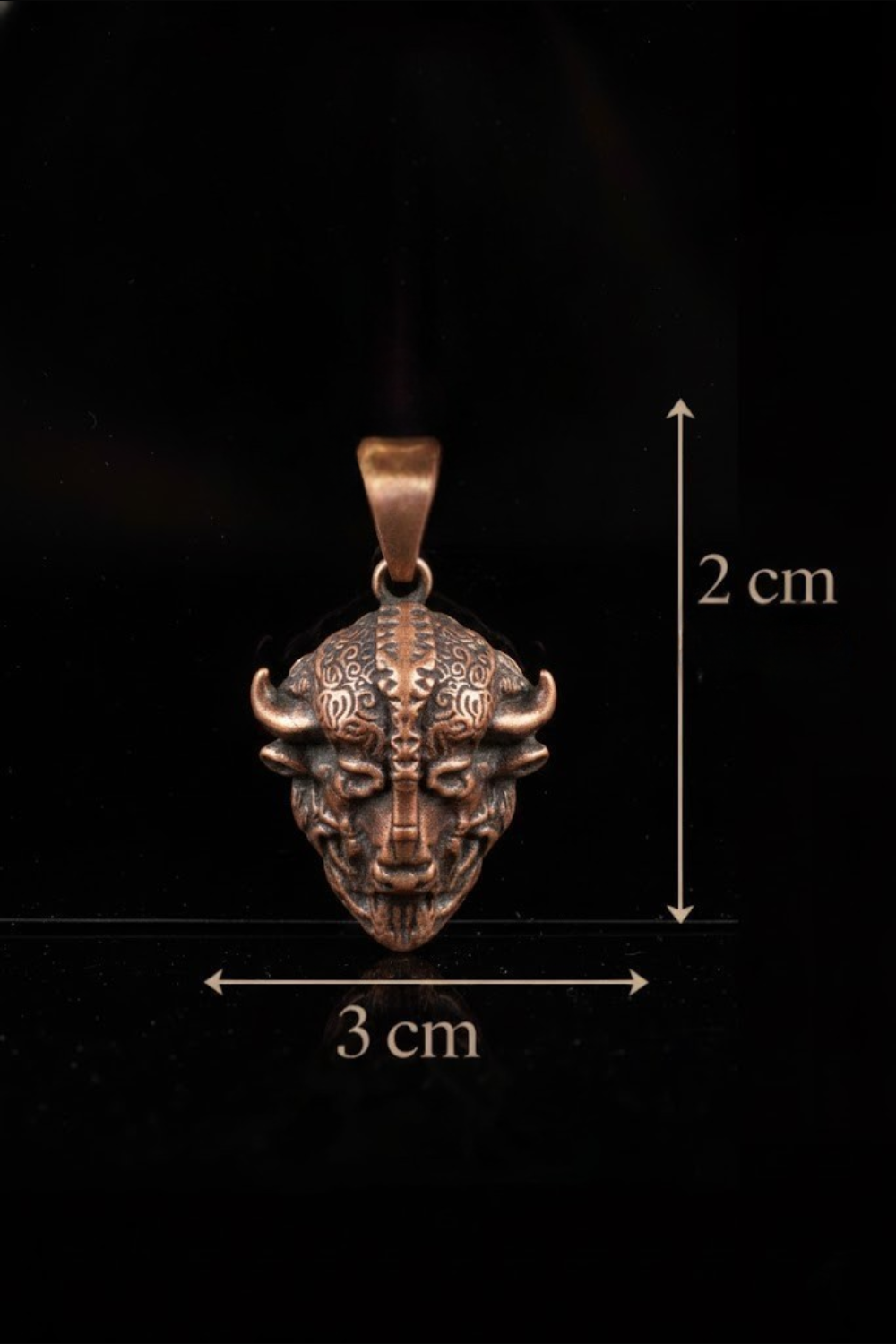 A pendant in the shape of a bull's head, with intricate designs and details, is shown against a black background.