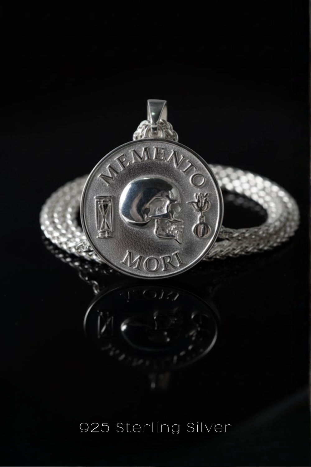 A silver medallion with the text "MEMENTO MORT" engraved on it, surrounded by a silver chain.