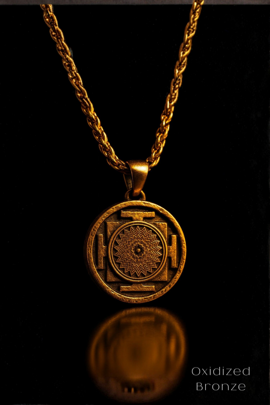 A gold-colored pendant with a circular design featuring a sun-like motif, suspended from a chain against a black background.