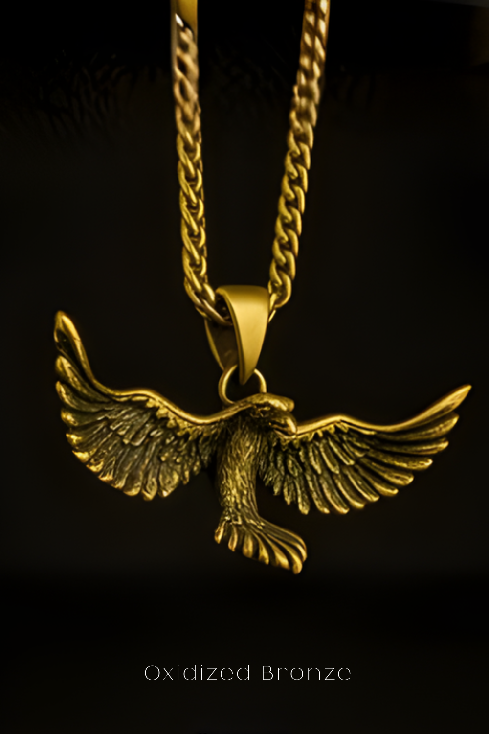 A close-up view of a gold-colored pendant in the shape of a bird, with its wings spread wide, against a dark background.