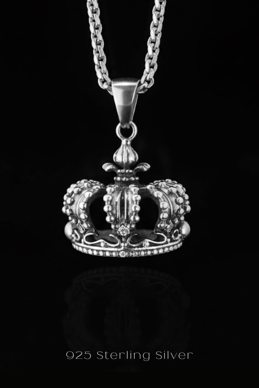 A silver-toned pendant necklace with a detailed crown-shaped pendant against a black background.