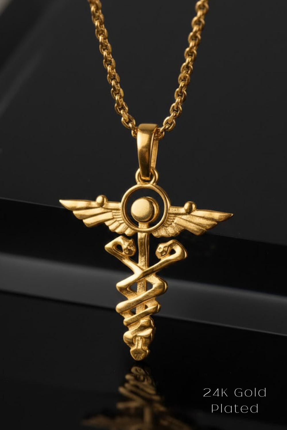 A 24K gold plated pendant in the shape of a medical symbol, possibly a caduceus, is displayed against a black background.