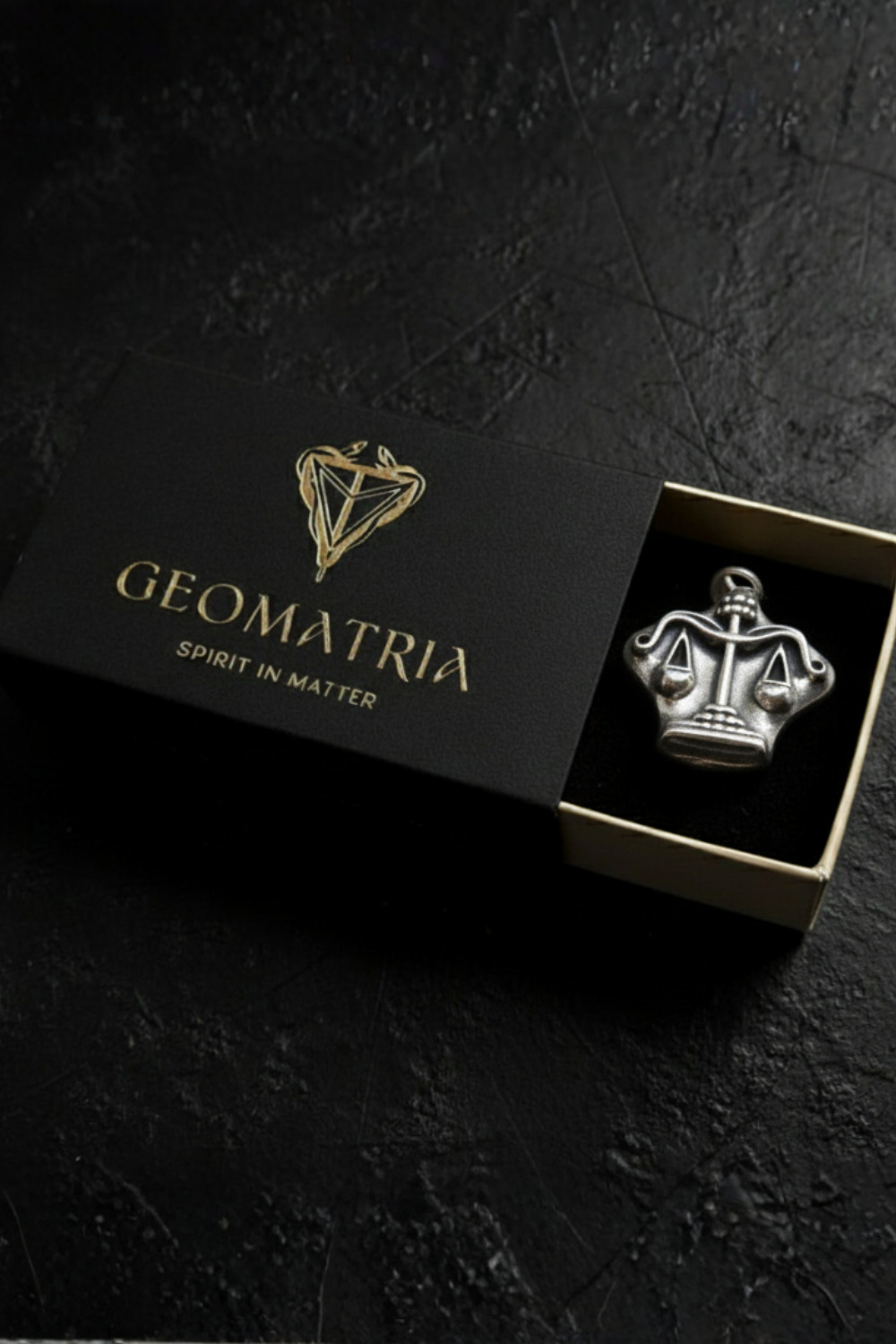 A black box with a gold logo and the word "Geomatria" on it, along with a silver emblem of a crown inside the box.