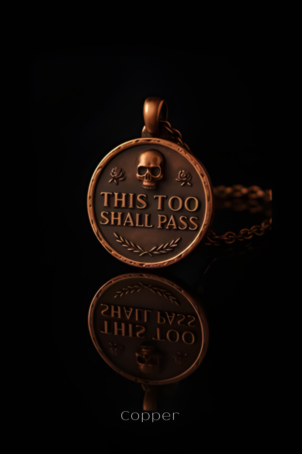 A copper-colored pendant with the text "THIS TOO SHALL PASS" engraved on it, along with a skull and rose design.
