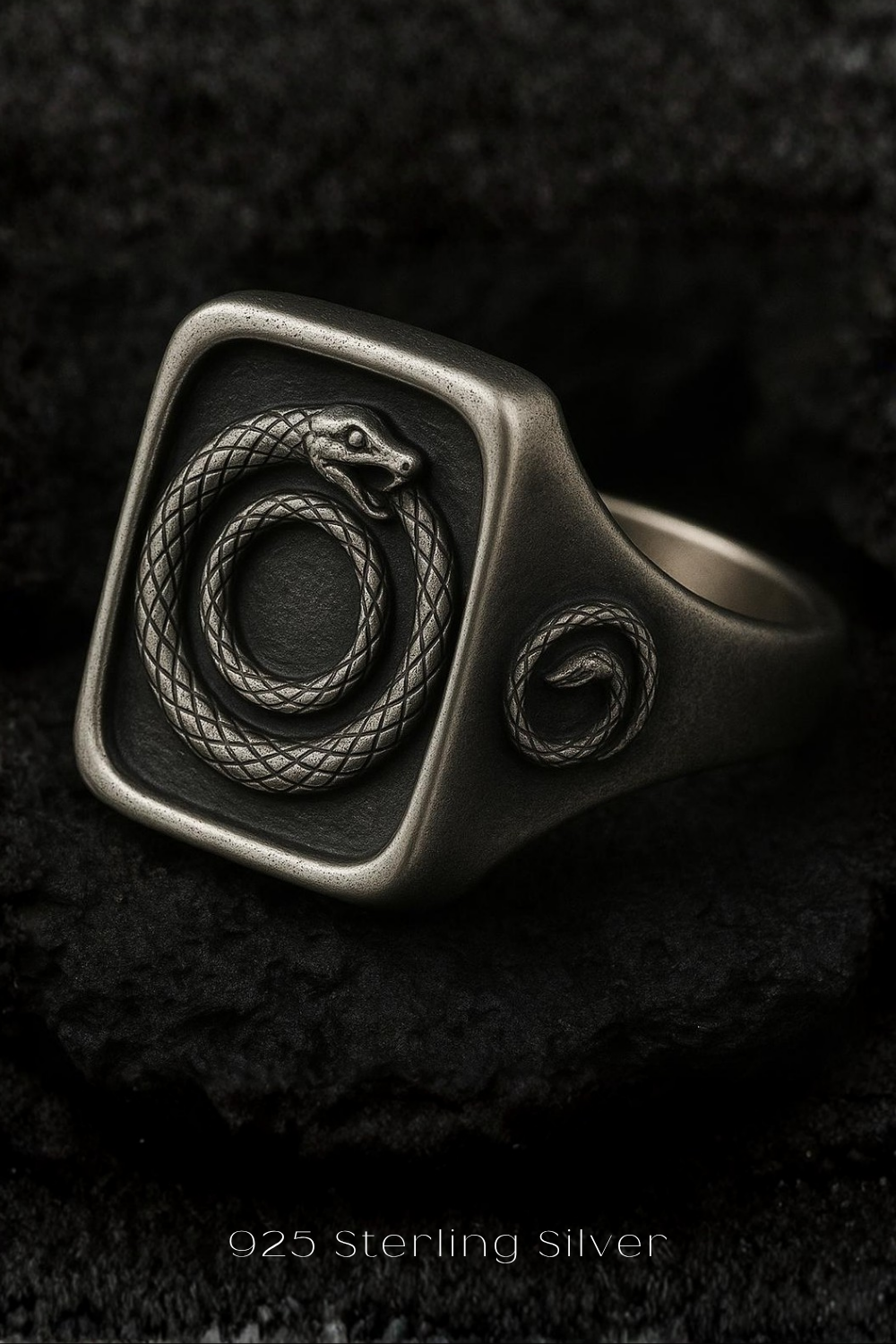 A silver ring with a snake design on the front, resting on a dark surface.