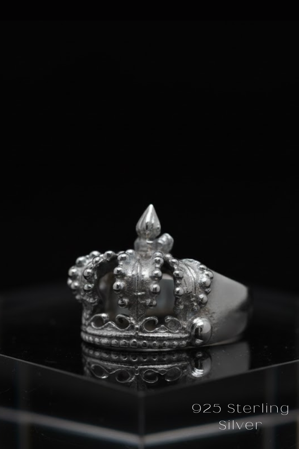 A silver crown ring with a pointed top and intricate designs, displayed against a black background.