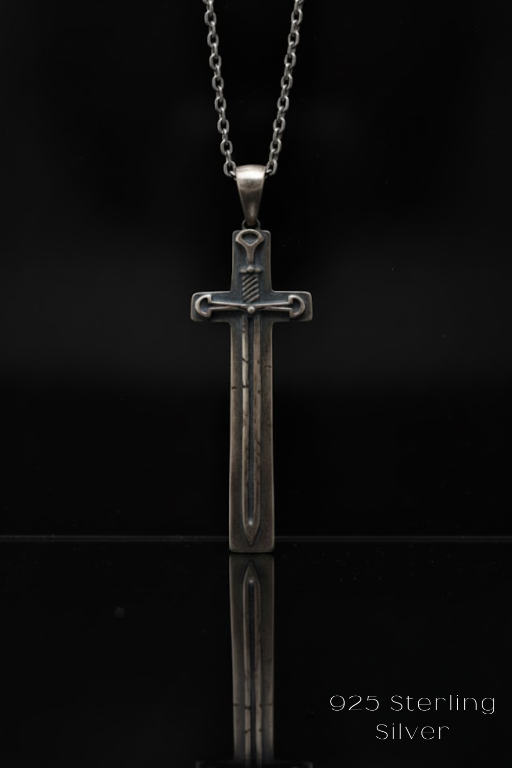 A silver cross pendant with a sword design, displayed against a black background.