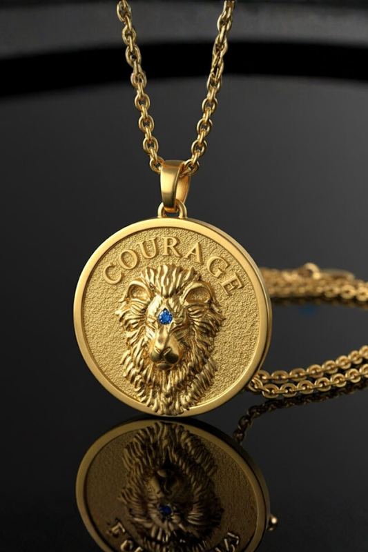 A gold-colored pendant necklace with a lion's head design and the word "COURAGE" engraved on it.