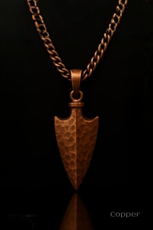 A copper-colored pendant with a textured, hammer-like design is suspended from a chain against a black background.