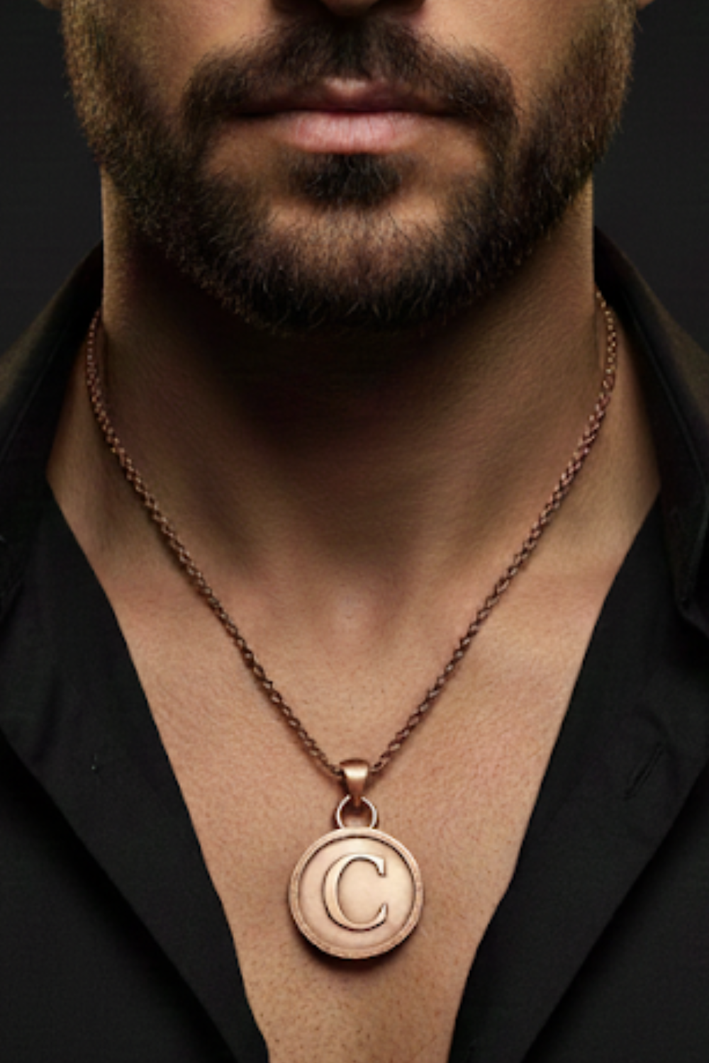 A close-up of a man's neck and chest area, with a necklace featuring a large circular pendant with the letter 'C' on it.