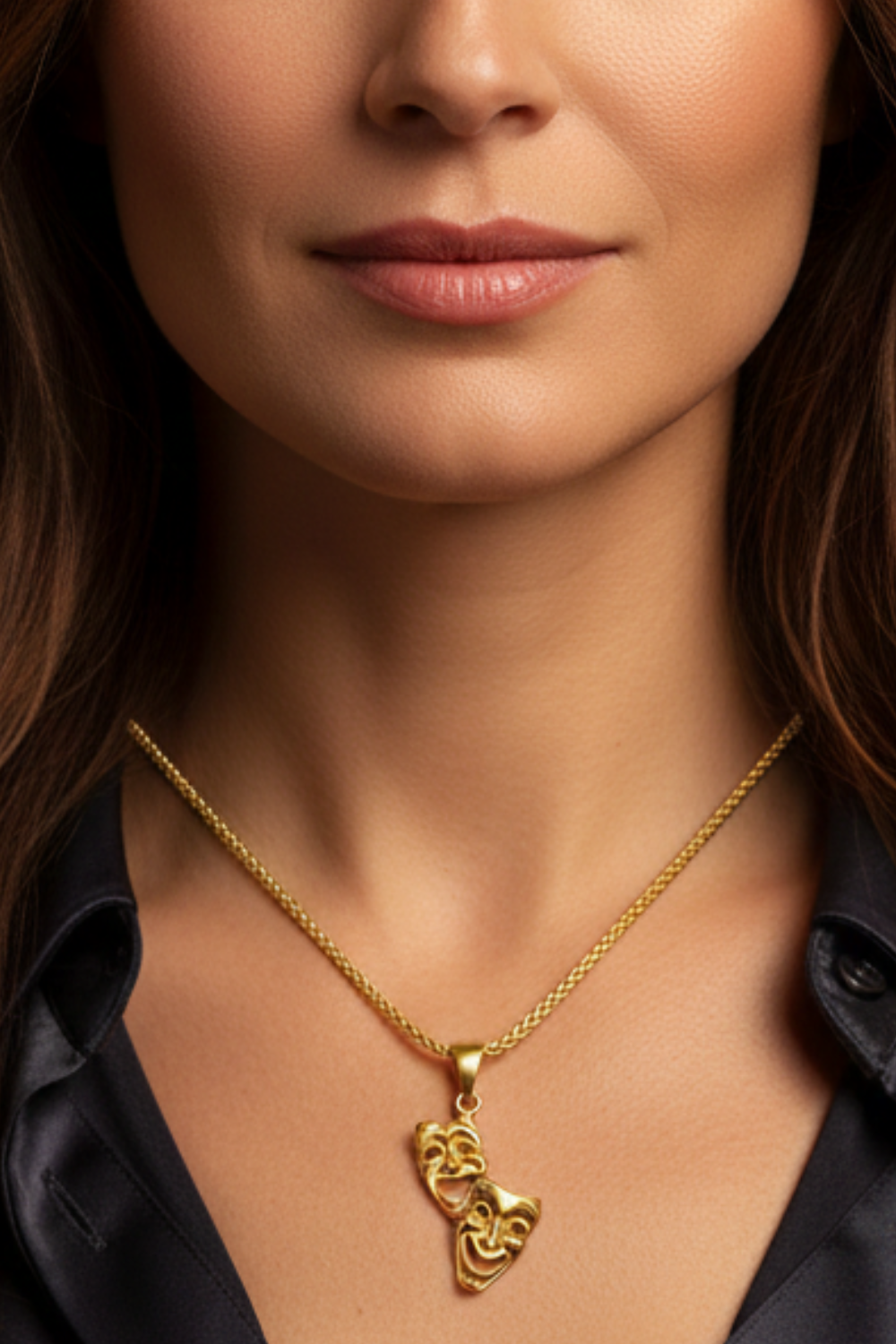 A close-up of a woman's neck and chest area, with a gold necklace featuring a pendant with theatrical masks.