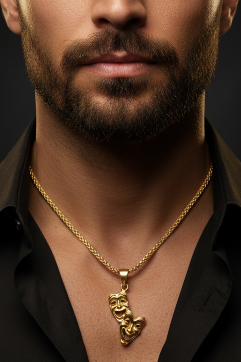 A close-up of a man's neck and chest area, with a gold chain necklace featuring a pendant with two theatrical masks.